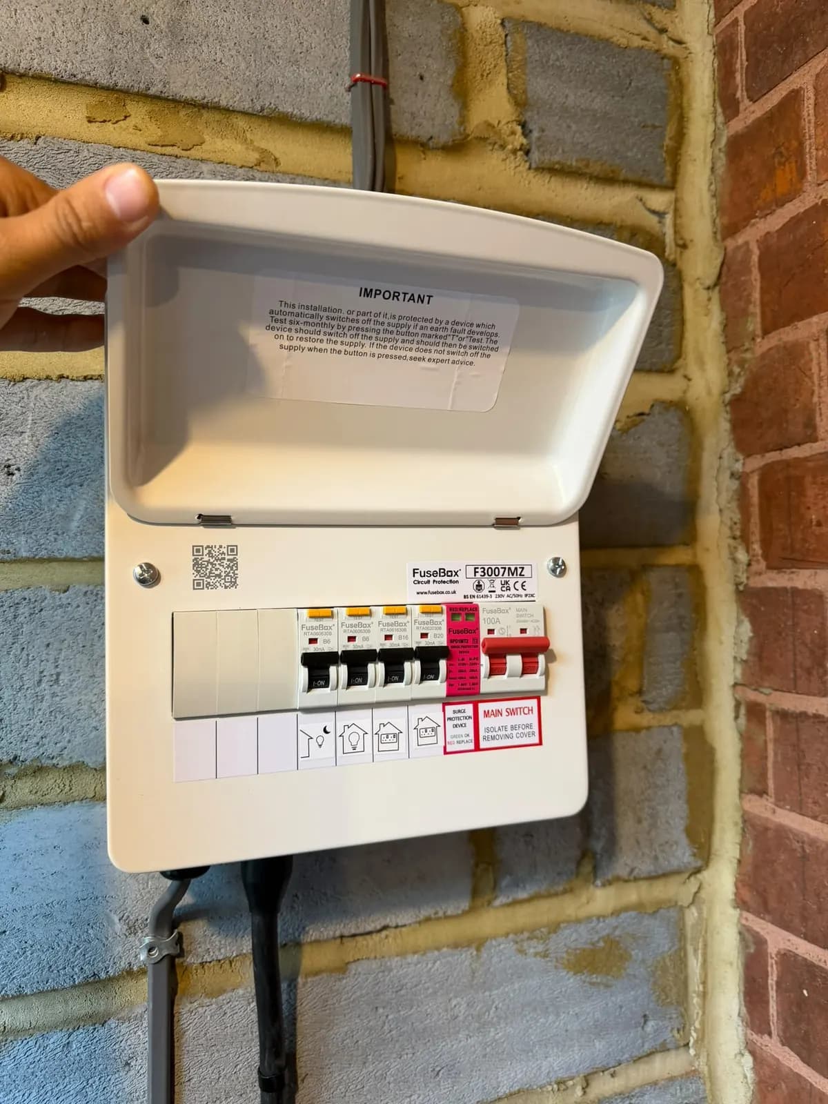 New consumer unit with main switch and breakers on a block wall in Salfords