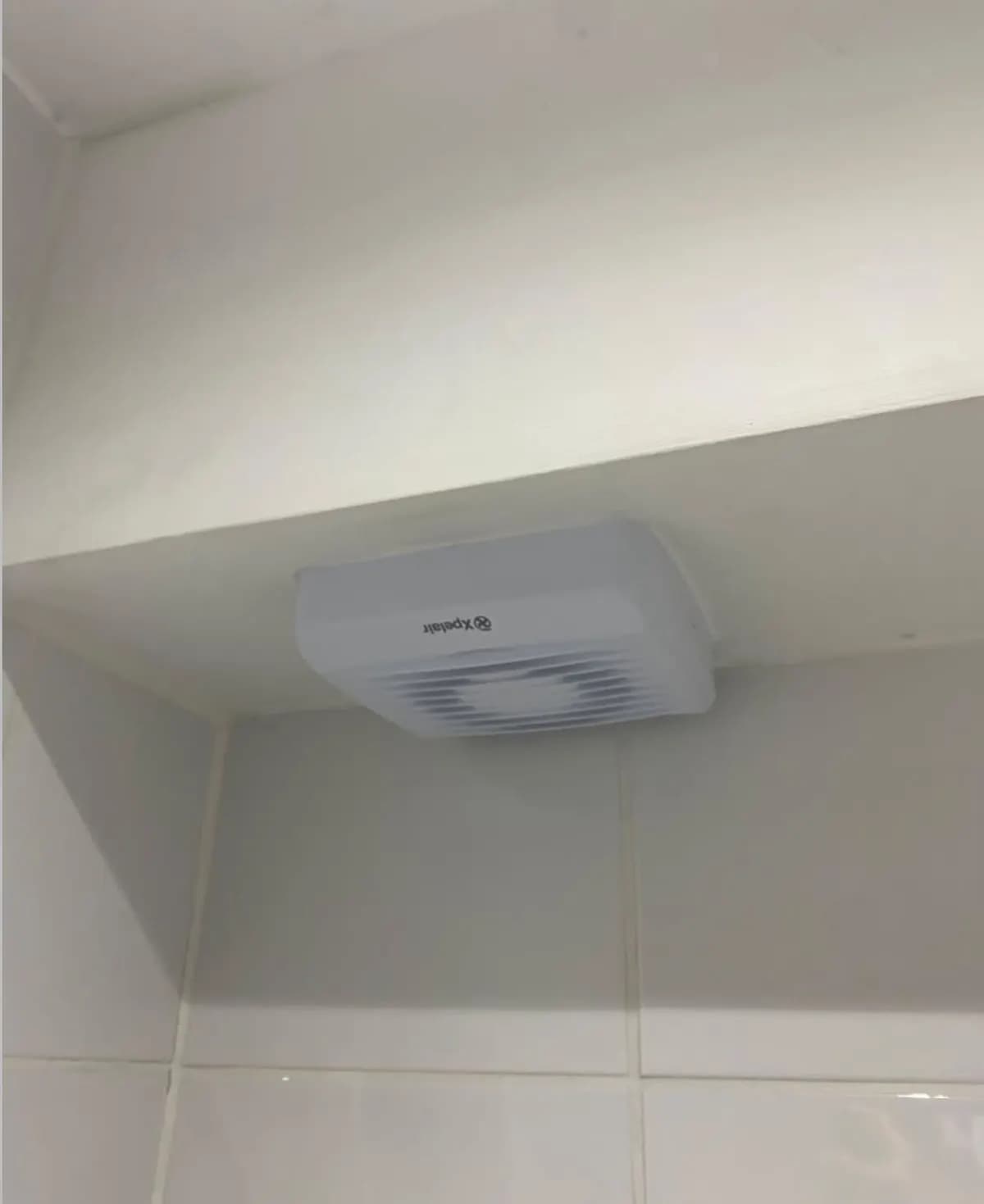 New white extractor fan fitted neatly in a tiled bathroom in Redhill